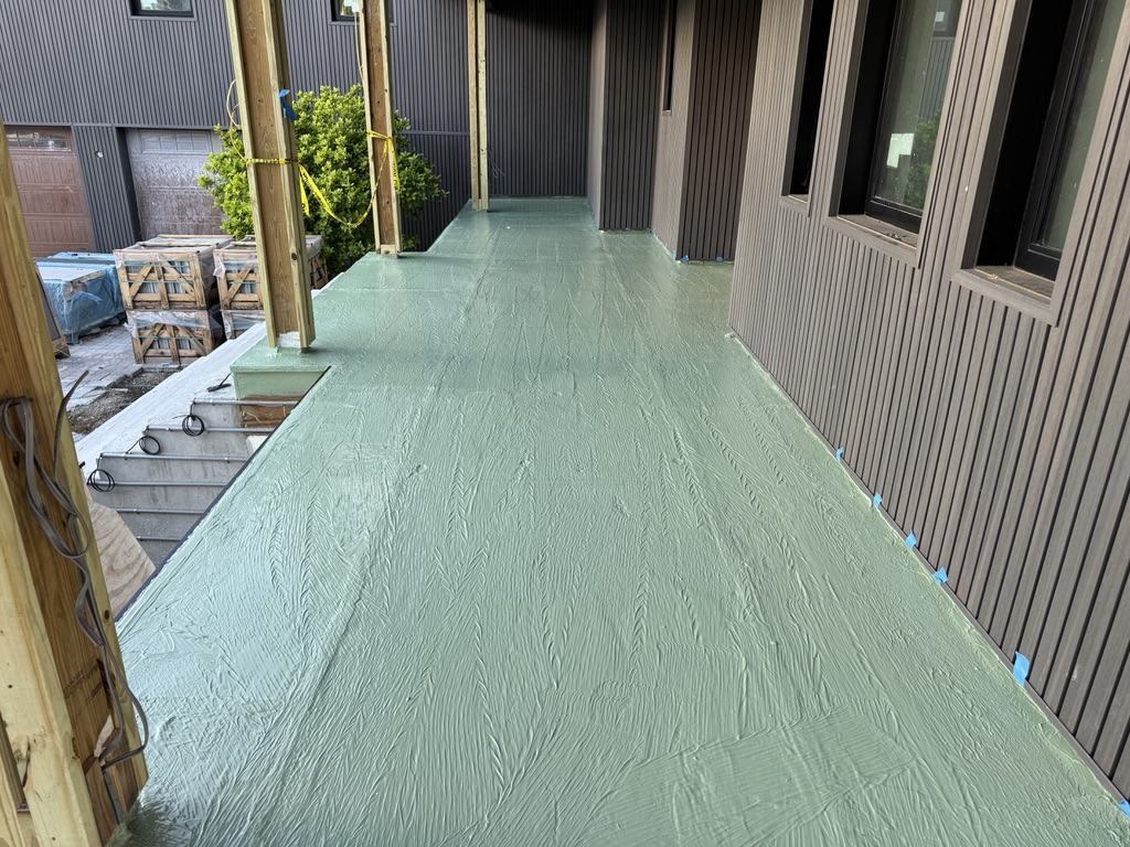 Coated elevated walkway deck running alongside vertical siding, coating carried up the wall base